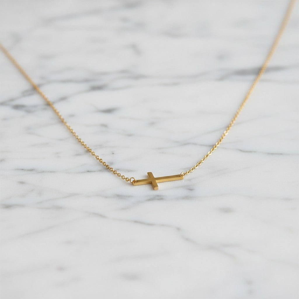 KM Jewelry Co. polished 18k gold PVD stainless steel horizontal cross necklace on mossy ground with ferns and flowers.